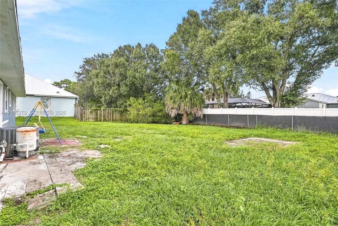 Backyard featuring a grass lawn, perimeter vinyl fencing, and mature trees