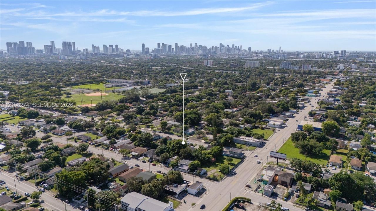 Aerial perspective featuring a residential lot with mature trees, situated within proximity to urban skyline infrastructure and local park grounds