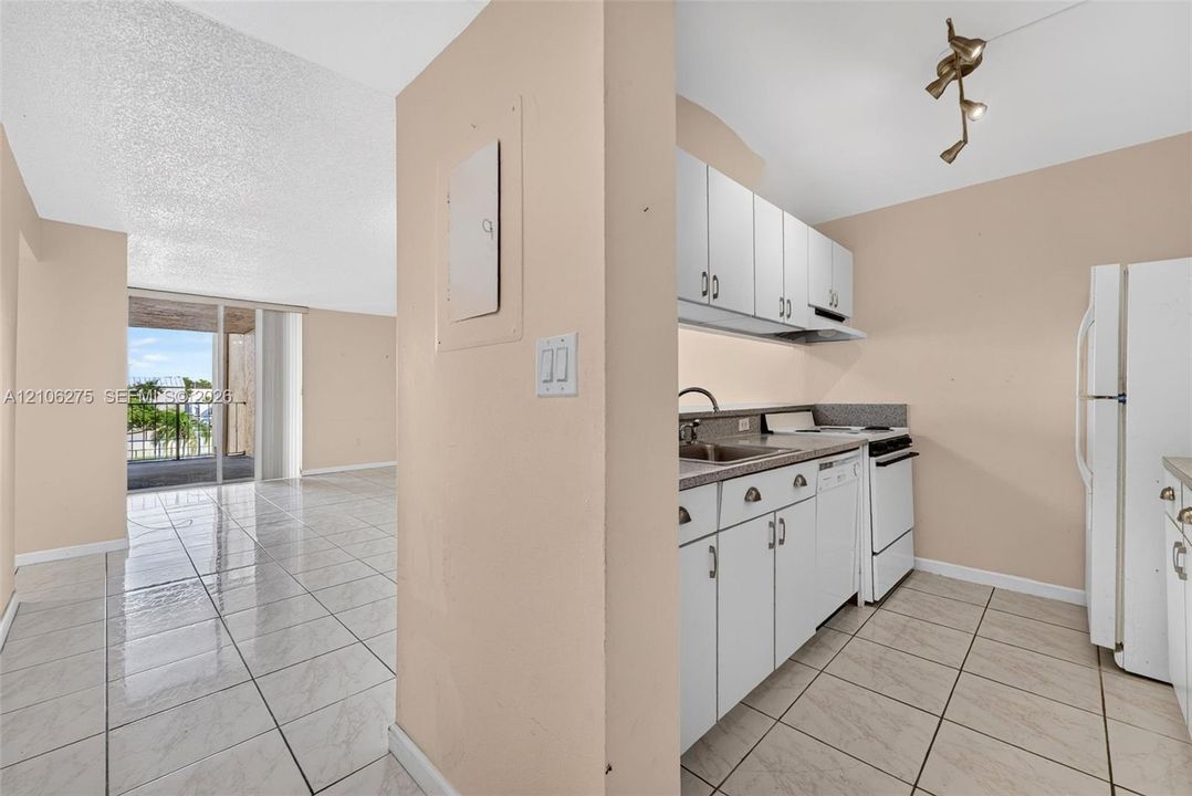 Kitchen featuring white cabinetry, stone-finish countertops, tile flooring, and integrated lighting, with tile flooring extending throughout the main living space