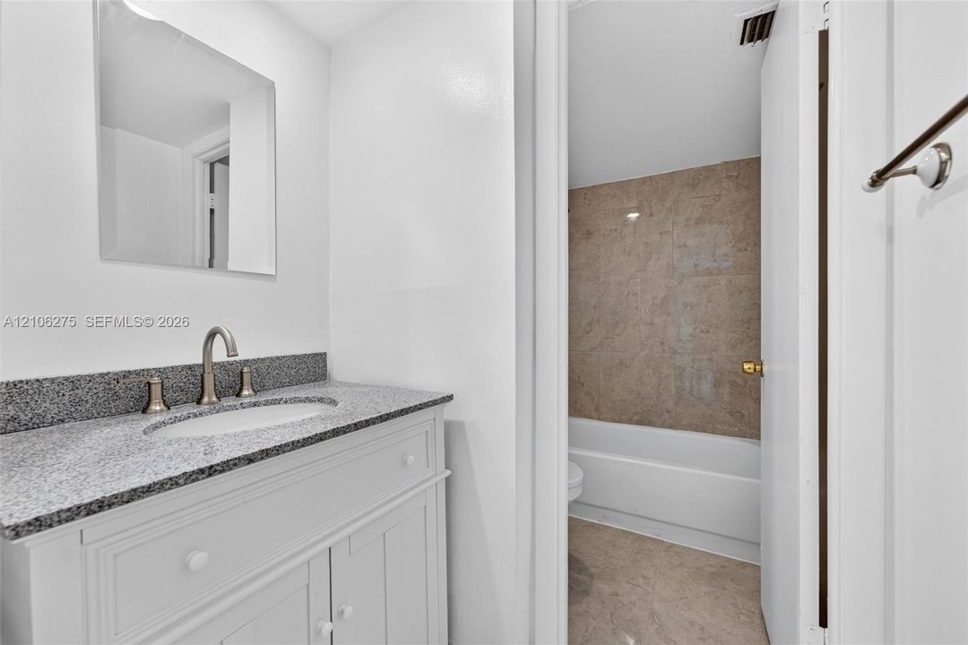 Bathroom featuring a vanity with stone-finish countertop, undermount sink, brushed nickel faucet, wall-mounted mirror, and a tile-surround shower and tub combination
