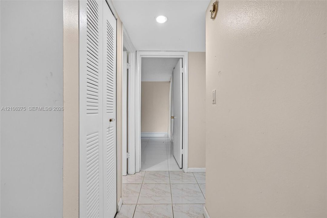 Hallway featuring white floor tiling, recessed lighting, and a white louvered closet door