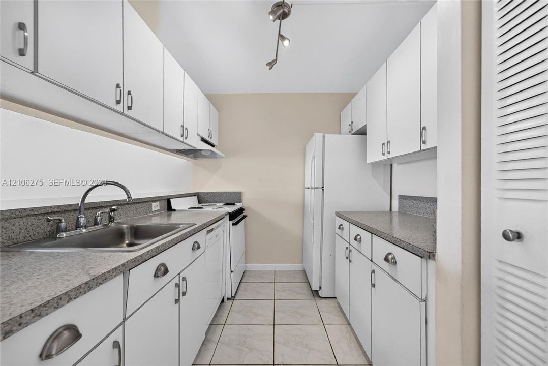 Kitchen featuring white cabinetry, stone-finish countertops, stainless steel sink with arch-neck faucet, ceramic tile flooring, and integrated white appliances