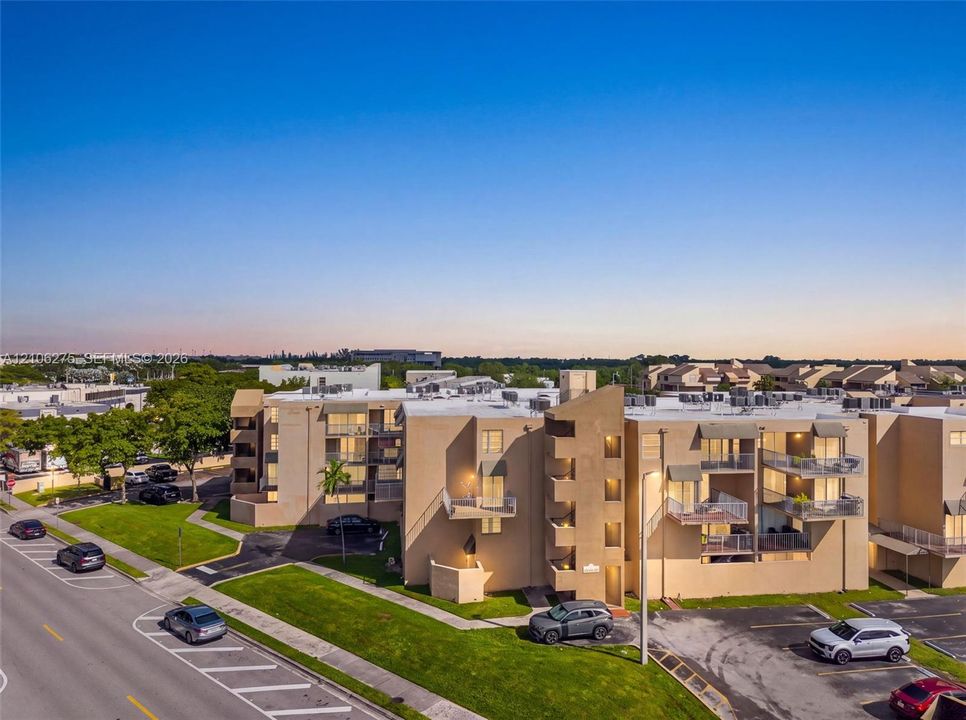 Multi-story residential complex featuring stucco exterior walls, private balconies with metal railings, and asphalt parking areas