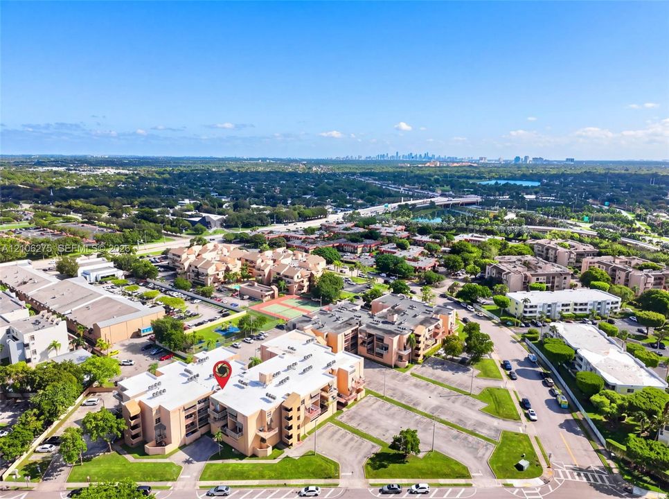 Aerial perspective of a multi-story residential complex featuring paved surface parking, manicured landscaping, and proximity to municipal roadways