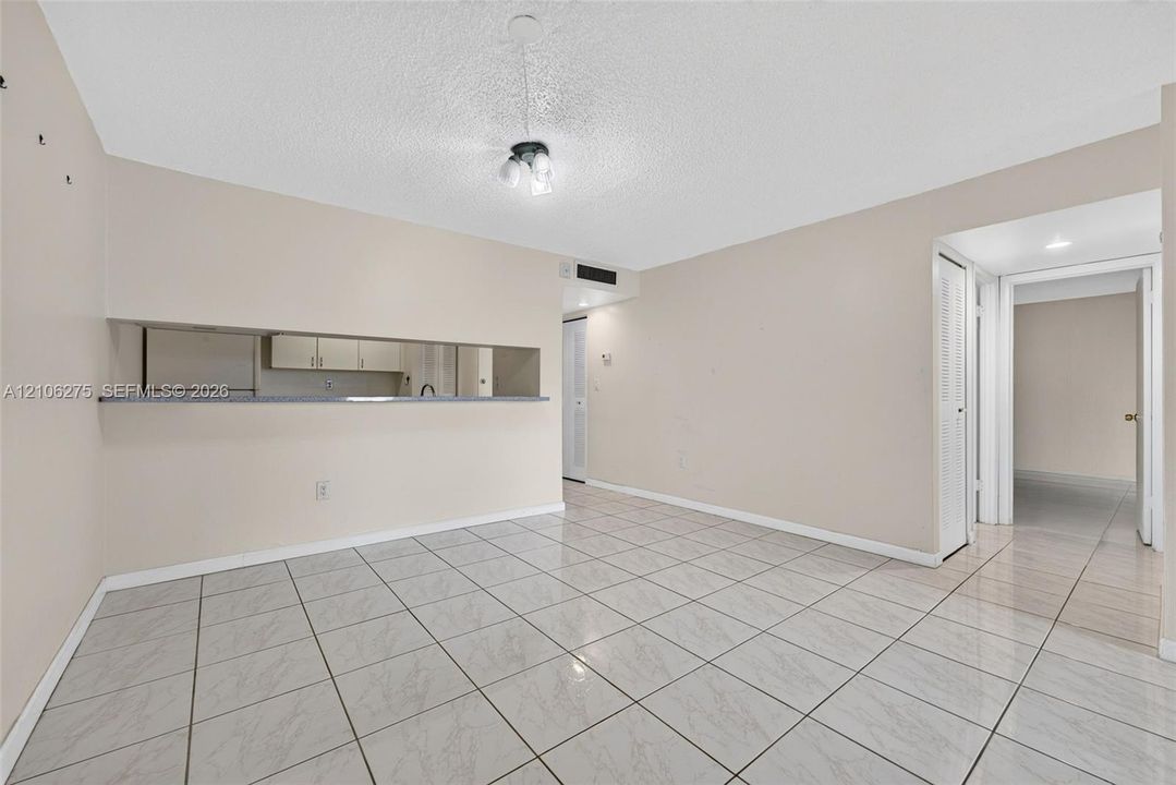 Open interior space featuring light-toned tile flooring, neutral wall paint, a pass-through opening to the kitchen, and a flush-mount ceiling fixture