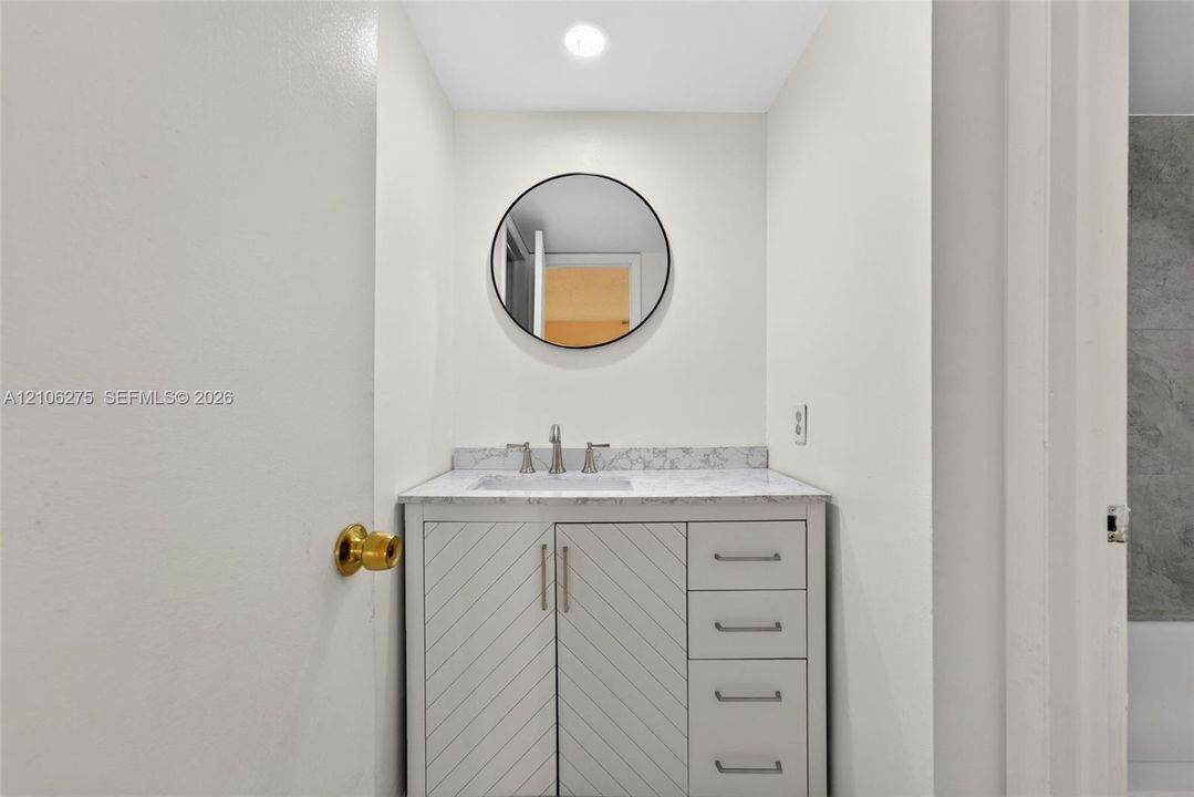 Vanity with stone-finish countertop, undermount sink, chevron-pattern cabinet doors, metallic hardware, and circular wall-mounted mirror
