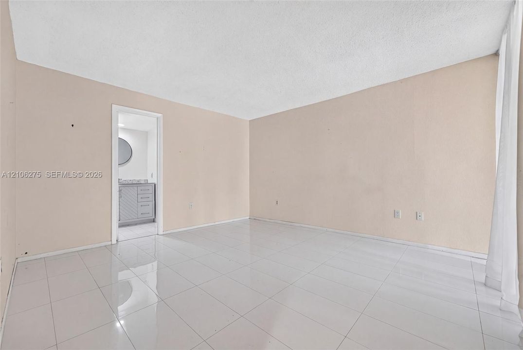 Interior room featuring light-toned neutral wall paint, polished tile flooring, and a doorway revealing a built-in vanity with cabinetry