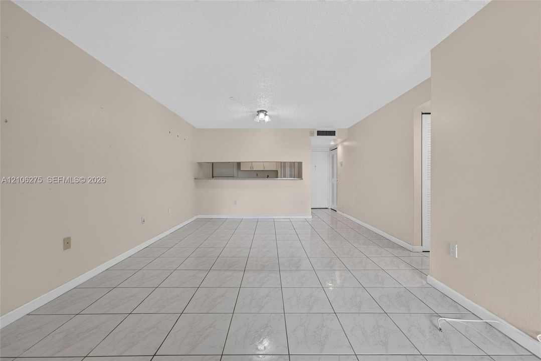 Neutral-toned interior space featuring light-colored tile flooring, a pass-through window opening, and a centralized ceiling-mounted light fixture