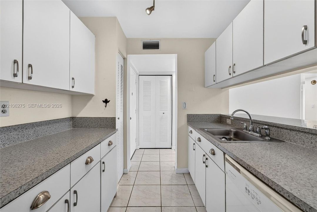 Kitchen featuring white cabinetry with metallic hardware, stone-composite countertops, stainless steel dual-basin sink, and ceramic tile flooring