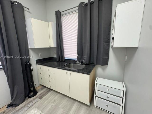 Custom cabinetry featuring a dark solid-surface countertop, stainless steel sink, and wall-mounted storage units set against light-toned wood-finish flooring