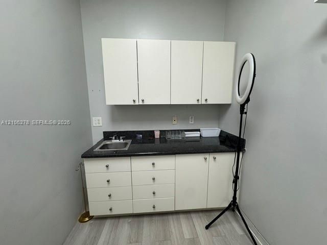 Built-in cabinetry featuring white shaker-style doors, dark solid-surface countertop, stainless steel drop-in sink, and wood-finish flooring