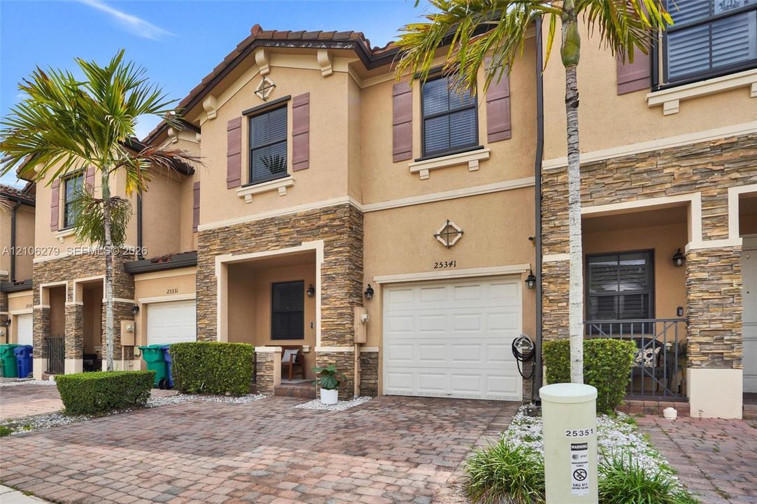 Two-story exterior featuring stucco siding, stone veneer accents, decorative shutters, a covered entryway, and a paved driveway