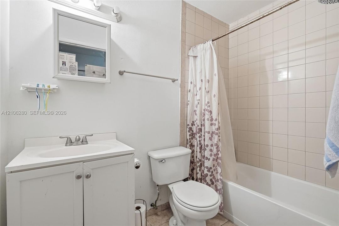 Bathroom featuring a white vanity cabinet with a drop-in sink, a wall-mounted medicine cabinet, a tiled shower surround, and a porcelain tub