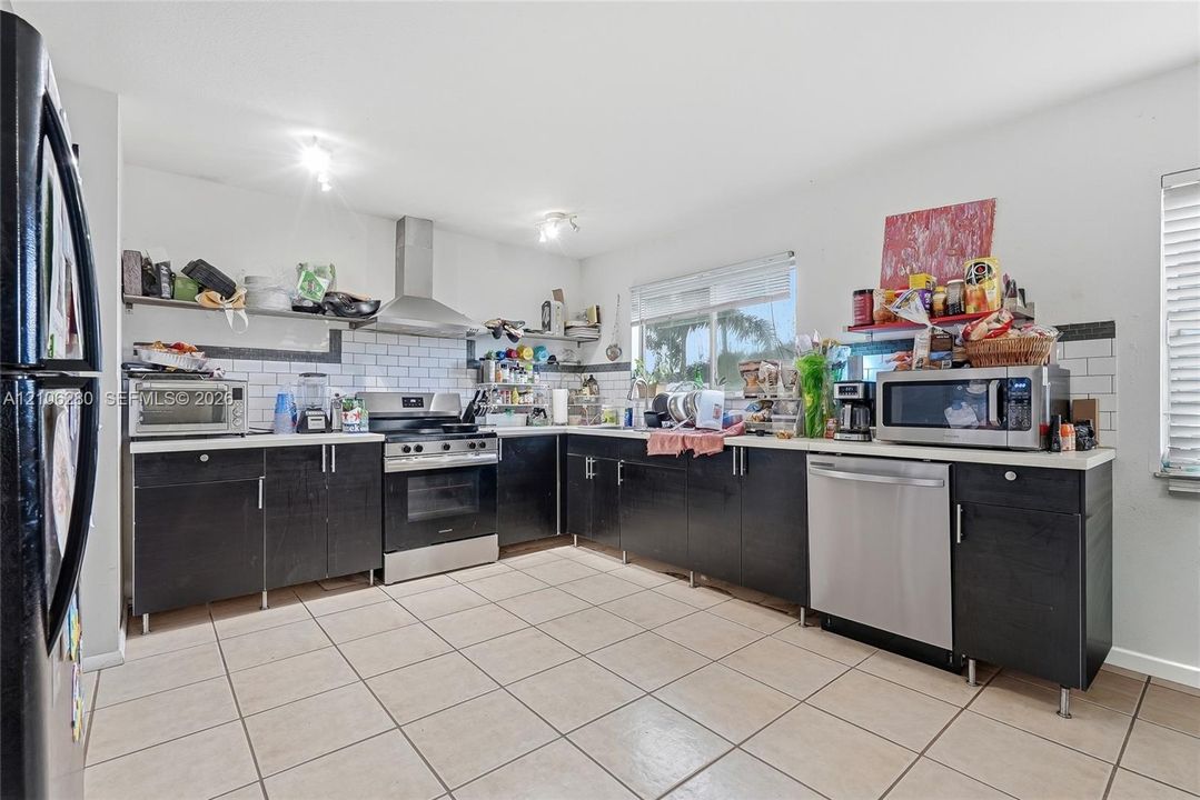 Kitchen featuring dark cabinetry, stainless steel appliances, a white tile backsplash, and ceramic tile flooring