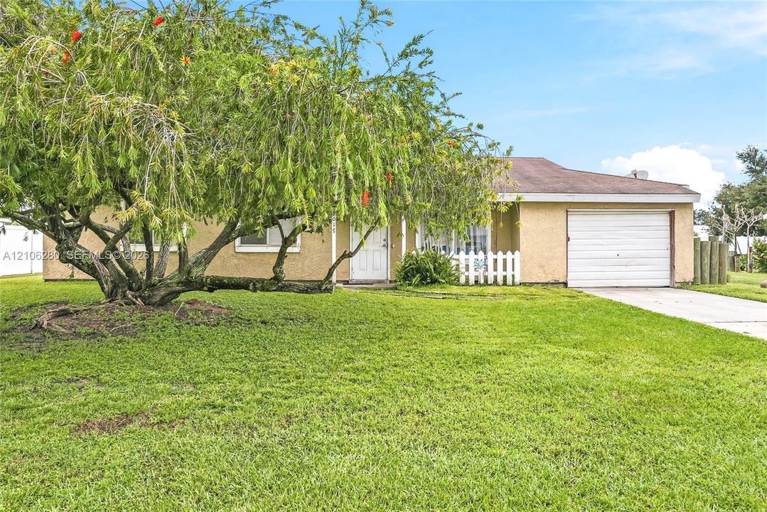 Stucco exterior featuring a concrete driveway, attached one-car garage, and picket fencing