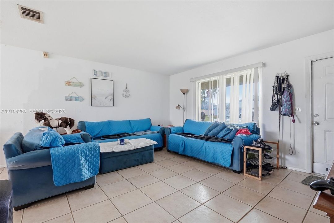 Living area featuring large-format tile flooring, neutral wall tones, and a multi-pane window with vertical blinds