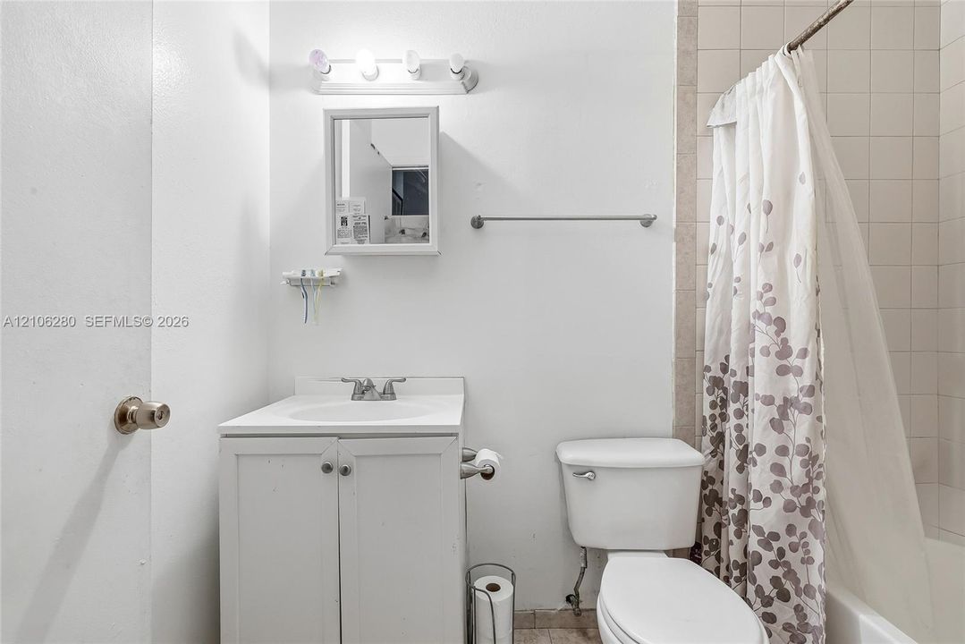 Bathroom featuring a white vanity with integrated basin, wall-mounted medicine cabinet, multi-bulb vanity light, and a tiled tub surround