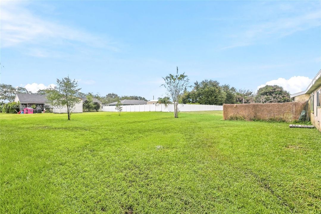 Expansive backyard featuring a manicured lawn, perimeter fencing, and mature trees
