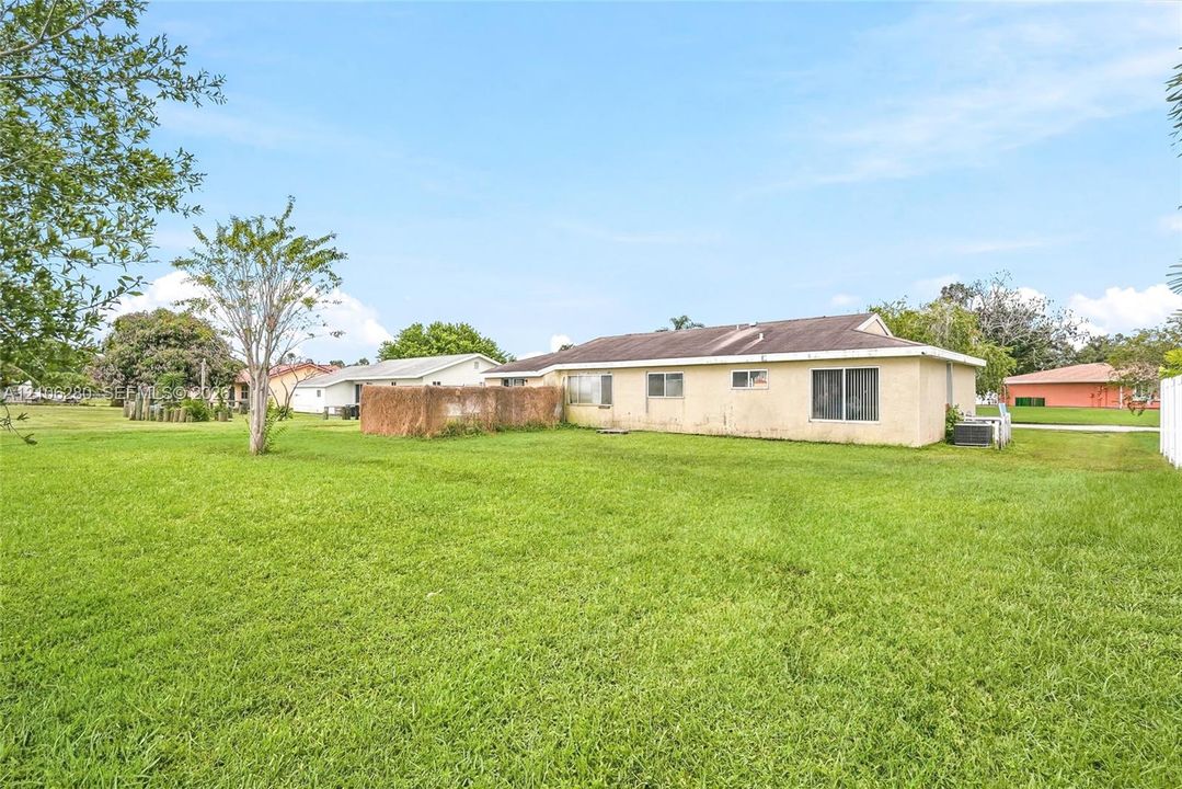 Expansive backyard featuring a large grass lawn, mature trees, and a textured exterior finish