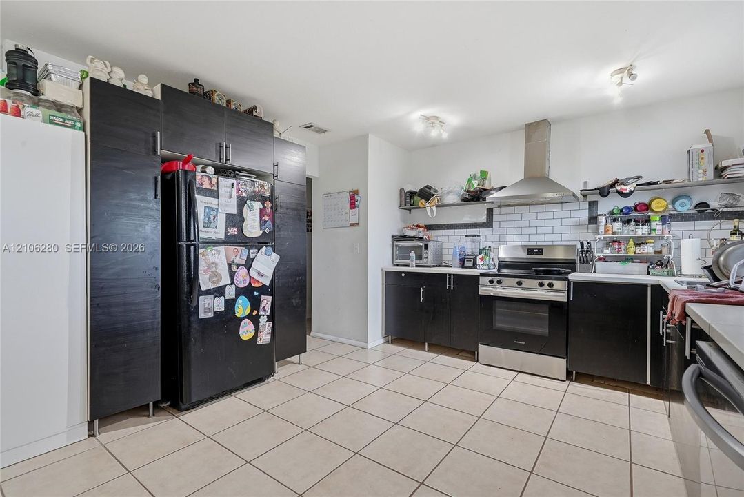 Kitchen featuring dark-finish cabinetry, stainless steel range with overhead vent hood, white subway tile backsplash, and light-tone tile flooring