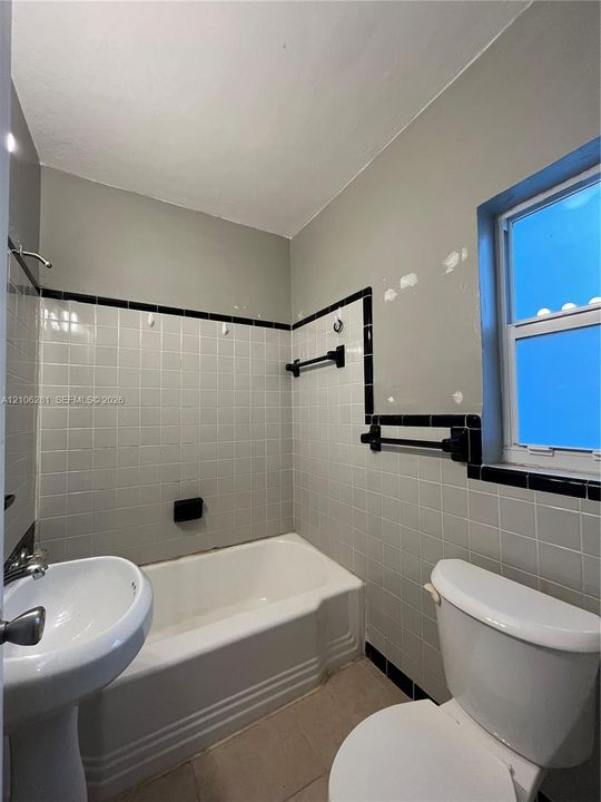 Bathroom featuring a white pedestal sink, a deep-basin soaking tub, square-tiled wall surround with decorative black trim, and wall-mounted towel hardware