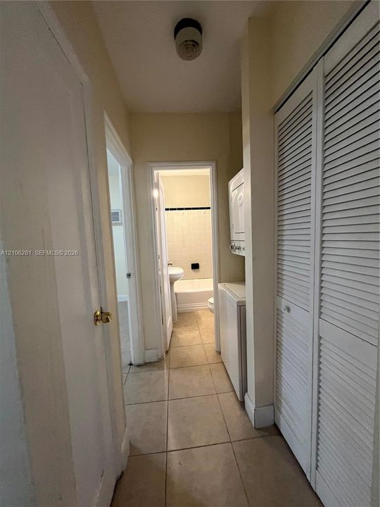 Utility area featuring large-format tile flooring, louvered bi-fold closet doors, and a stackable appliance unit