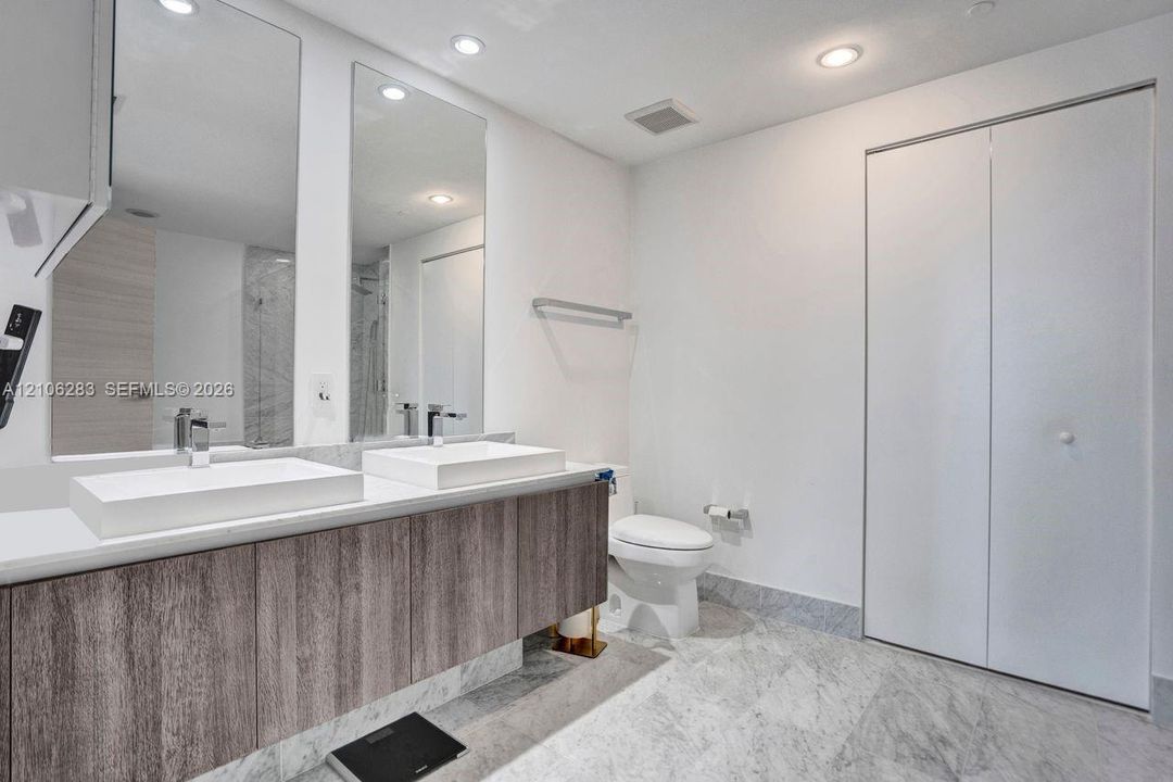 Floating vanity with dual rectangular vessel sinks, stone-finish flooring, full-height wall mirrors, and bifold closet doors