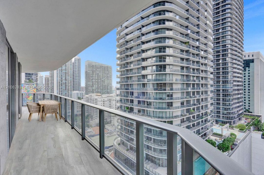 Covered balcony featuring wood-finish flooring and a glass-paneled railing with a metal handrail