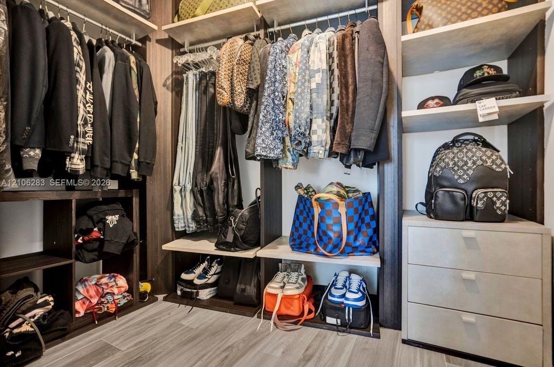 Custom walk-in closet featuring dark wood-finish shelving, multi-level hanging rods, built-in open cubbies, a three-drawer storage unit, and wood-finish flooring