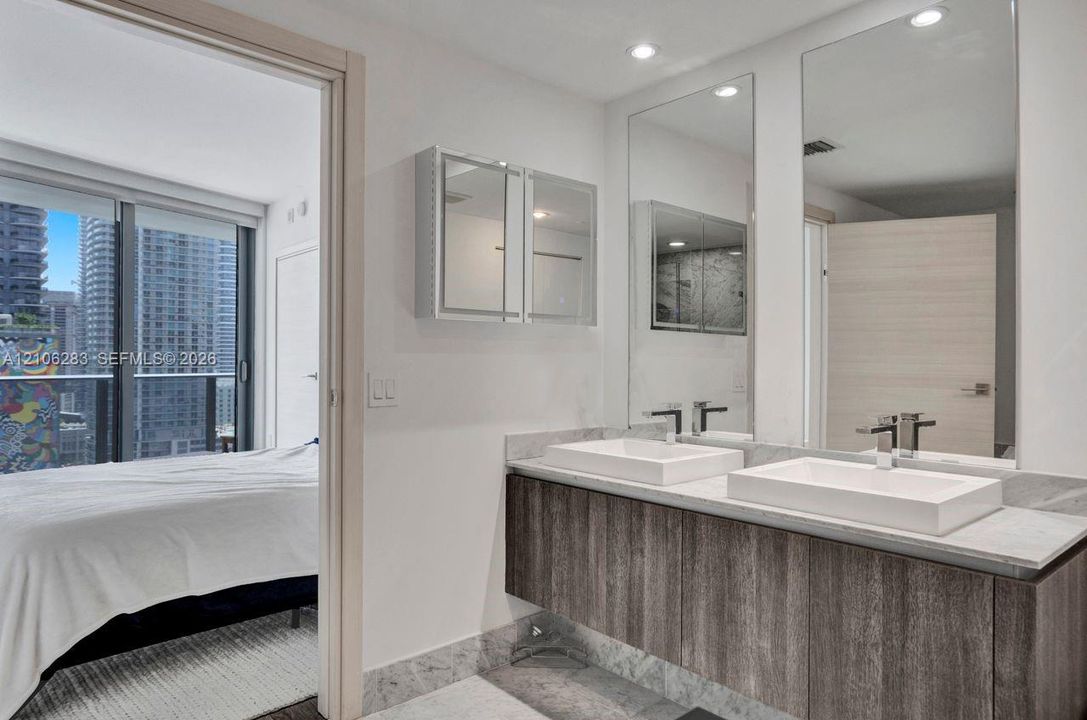 Floating wood-finish vanity with dual rectangular vessel sinks, stone-surface countertop, full-height wall mirrors, and recessed lighting