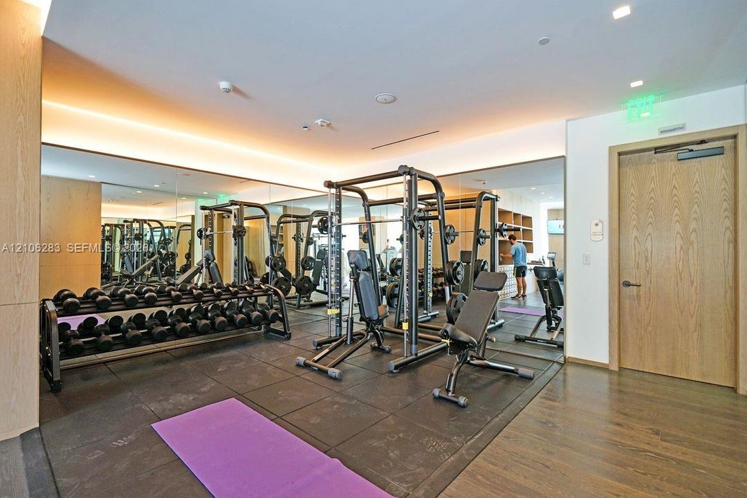 Fitness center featuring full-wall mirrors, recessed lighting, wood-finish wall paneling, and rubberized flooring