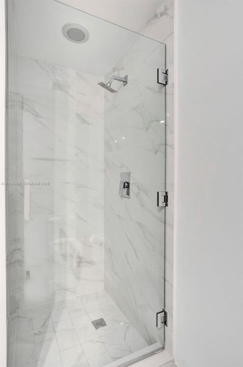 Walk-in shower featuring a frameless glass door, wall-to-wall stone-finish tile, recessed ceiling light, and polished chrome fixtures