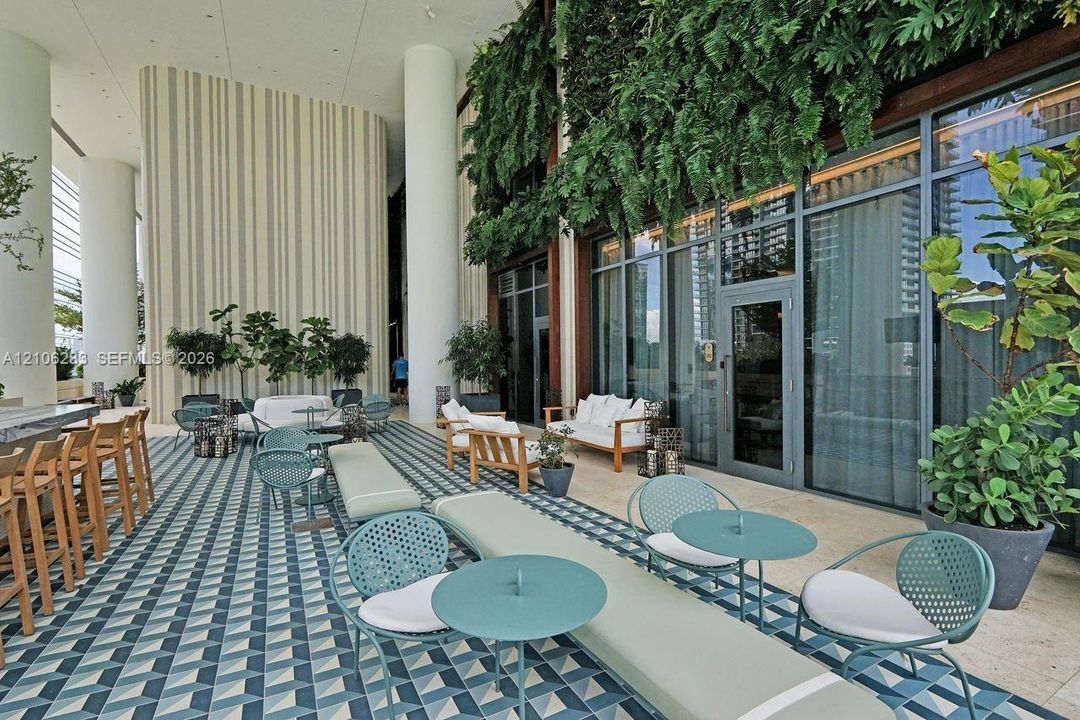 Covered outdoor terrace featuring geometric patterned tile flooring, floor-to-ceiling glass paneling, vertical green wall accents, and structural columns