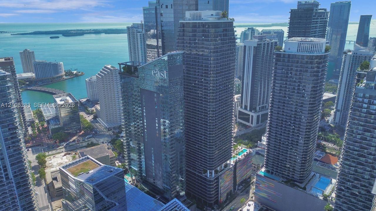 Aerial perspective of a high-rise urban skyscraper featuring floor-to-ceiling glass paneling, structured balconies, a rooftop pool, and proximity to the waterfront