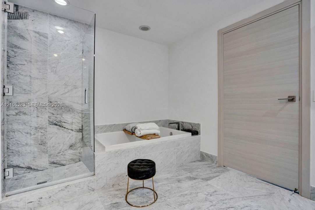 Frameless glass shower enclosure with stone tile surround, built-in soaking tub, stone tile flooring, and a light-toned wood-finish interior door