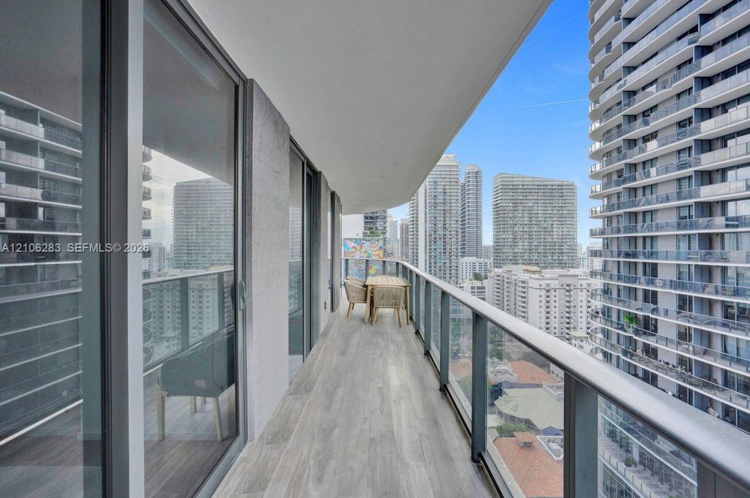Covered balcony featuring wood-finish flooring, full-height sliding glass doors, and a glass-paneled railing