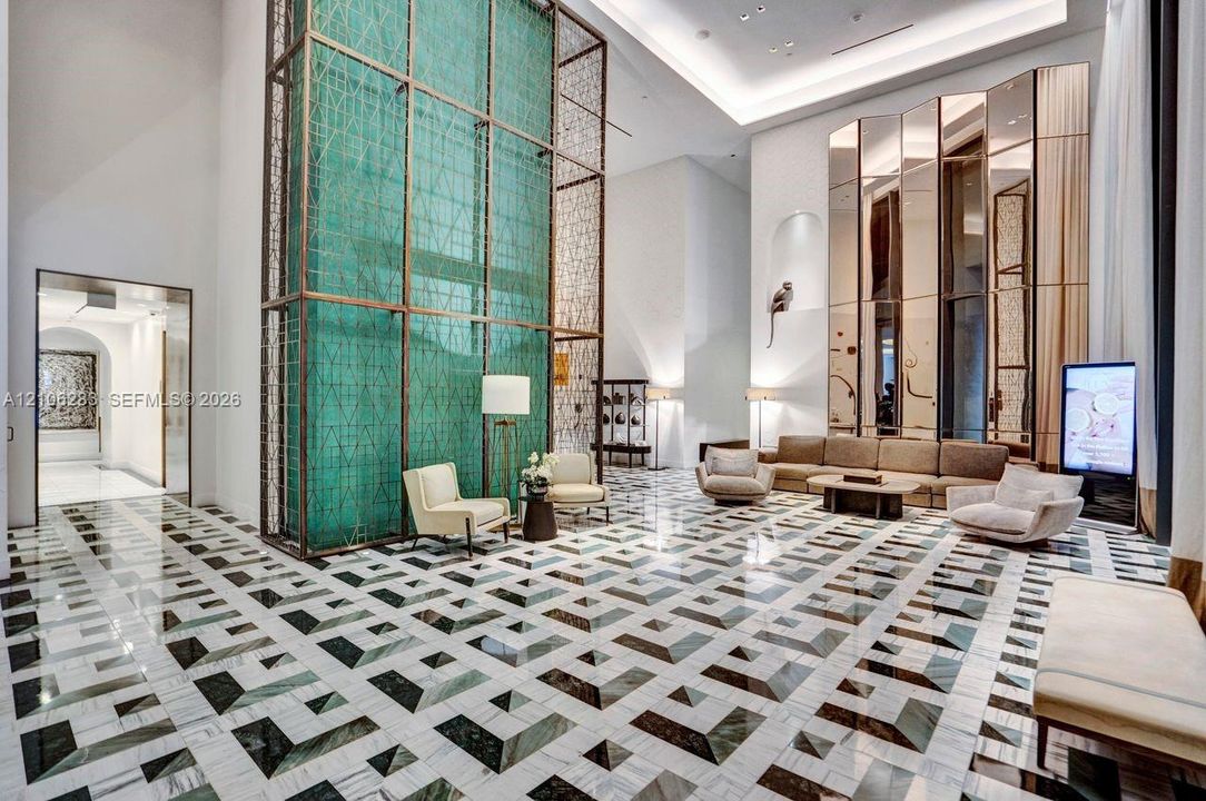 Grand lobby featuring double-height ceilings, a floor-to-ceiling metal latticework feature wall, geometric stone tile flooring, and full-height mirrored wall panels