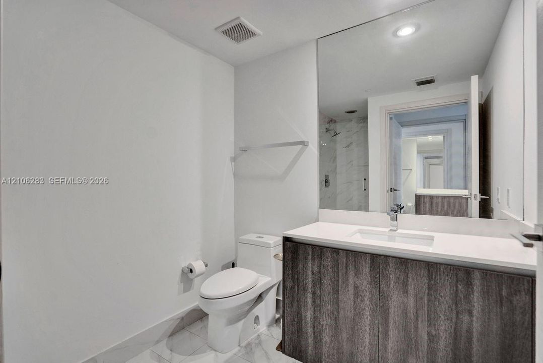 Modern vanity with dark wood-finish cabinetry, crisp white countertop, integrated rectangular sink, expansive wall-to-wall mirror, and stone-finish tile flooring