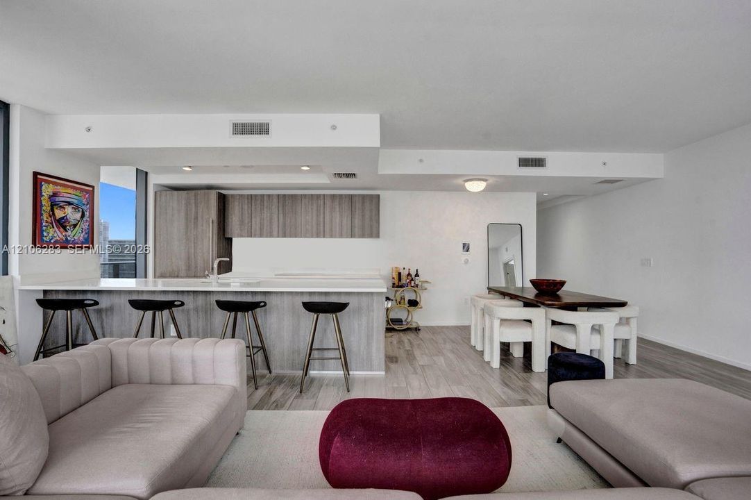 Open-concept living space featuring wood-finish flooring, a kitchen island with stone countertop, and contemporary flat-panel cabinetry