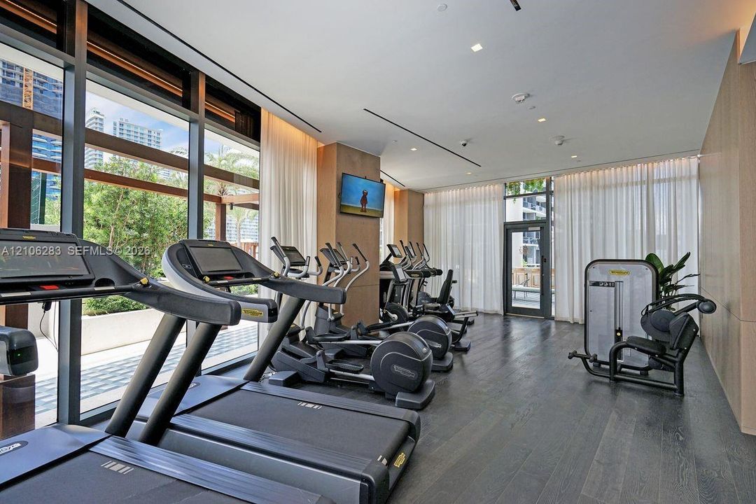 Fitness center featuring dark wood-finish flooring, floor-to-ceiling windows, recessed lighting, and wall-mounted neutral paneling