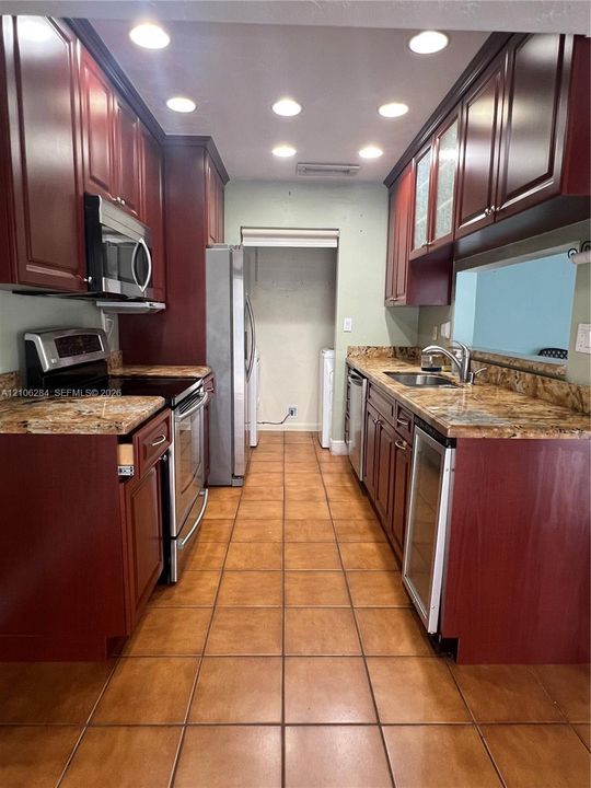 Kitchen featuring stained wood cabinetry, stone countertops, stainless steel appliances, a built-in wine refrigerator, and recessed lighting