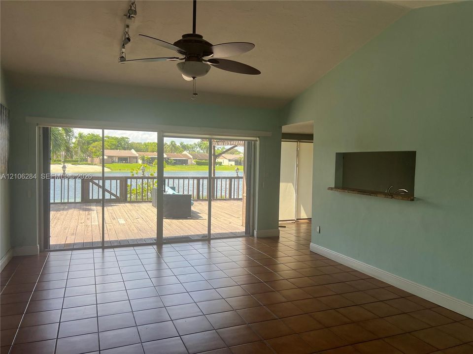 Ceramic tile flooring, vaulted ceilings, ceiling fan, pass-through window with shelf, and large sliding glass doors opening to a wood deck