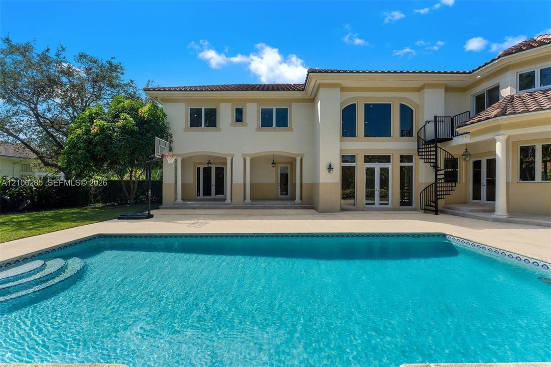 Stucco exterior featuring a covered patio, swimming pool with integrated steps, metal spiral staircase, and tile roofing