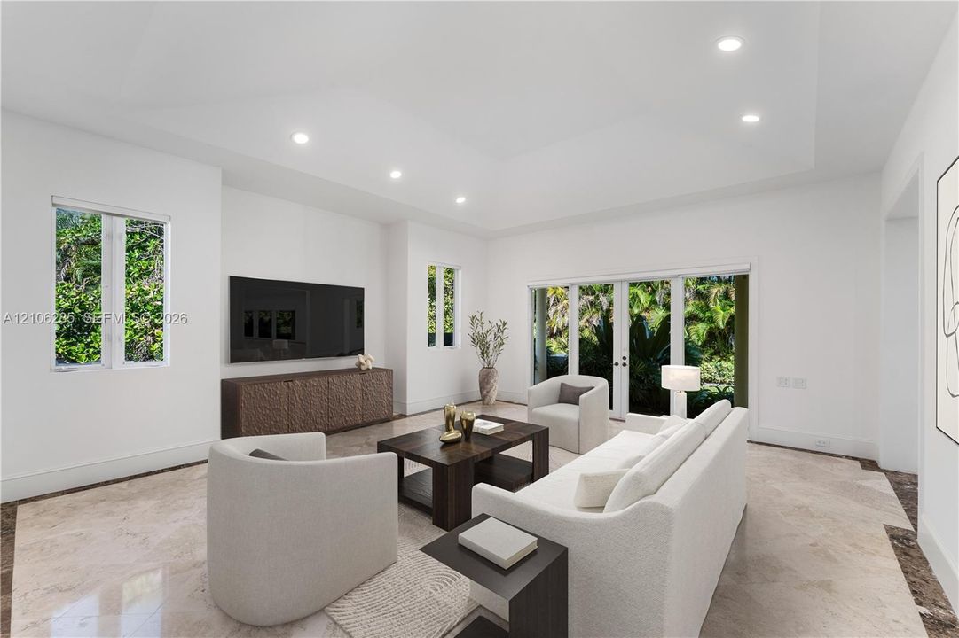 Living area featuring a tray ceiling, recessed lighting, stone flooring, and glass-paneled double doors with exterior access