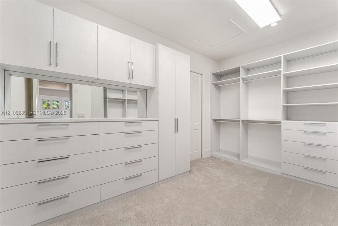 Custom built-in storage system featuring floor-to-ceiling cabinetry, multiple drawer banks, adjustable shelving units, integrated hanging rods, and a reflective mirror panel