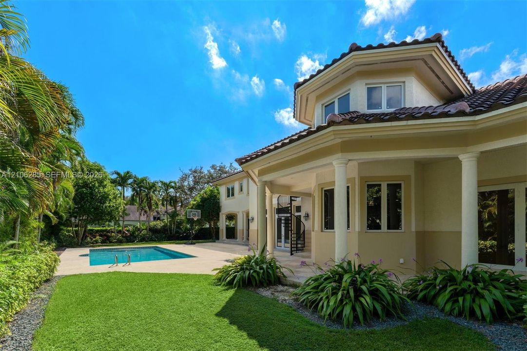 Stucco exterior featuring a wraparound covered patio, classical columns, a tile roof, an in-ground swimming pool, and a manicured lawn