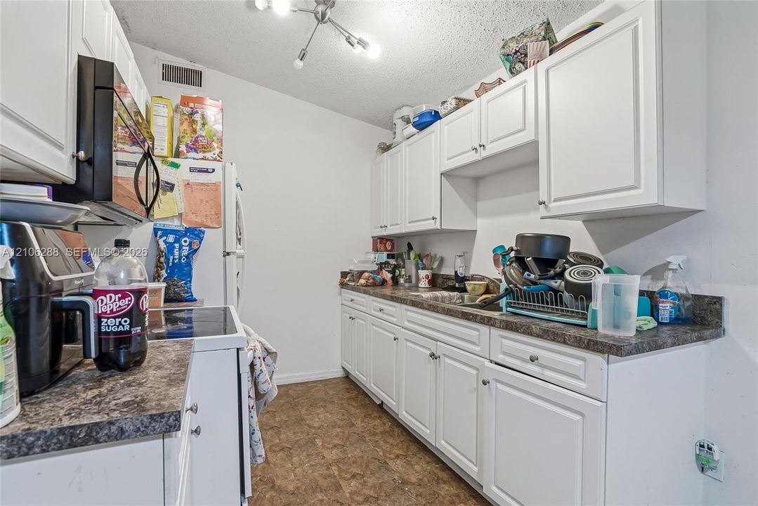 Kitchen featuring white shaker-style cabinetry, laminate countertops, a dual-basin stainless steel sink, and a multi-arm ceiling light fixture