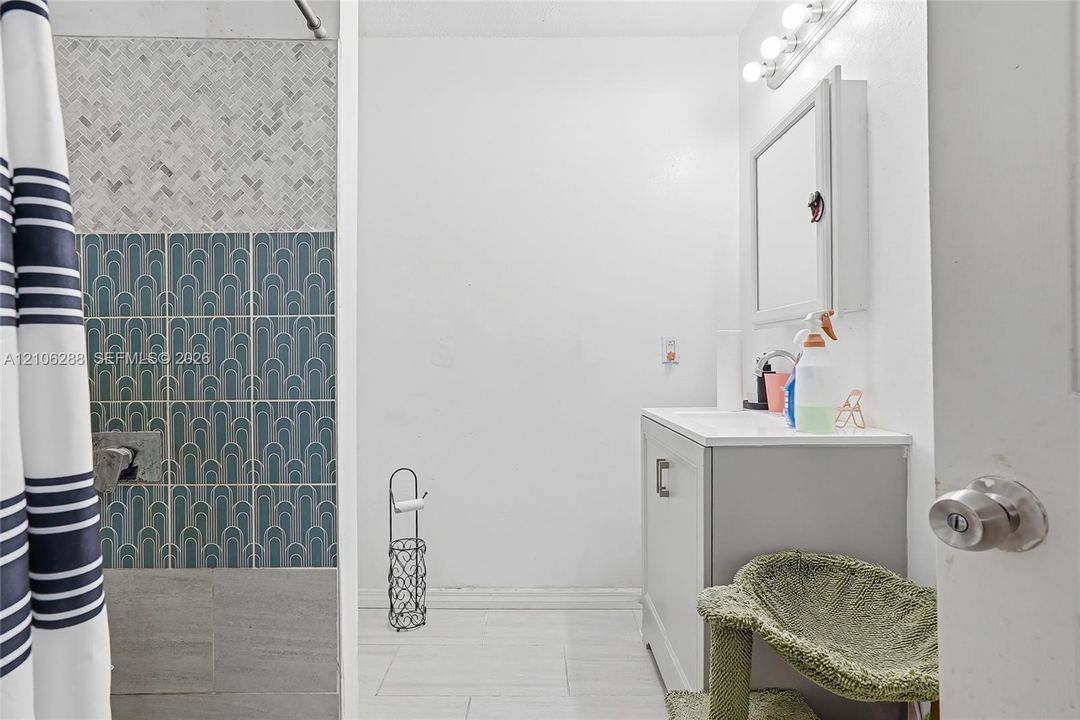 Bathroom featuring patterned wall tiling, light-tone floor tiling, a vanity with an integrated countertop, and a built-in mirrored medicine cabinet