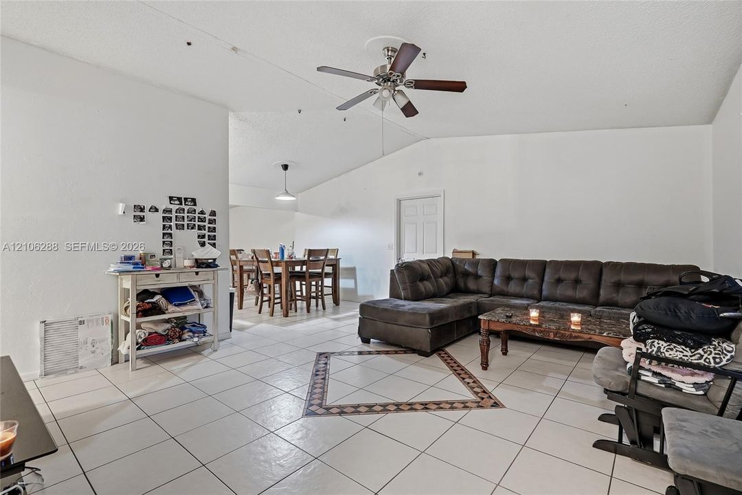 Open-concept interior featuring vaulted ceilings, light-toned ceramic tile flooring, a decorative inlaid floor mosaic, and a central ceiling fan with integrated lighting