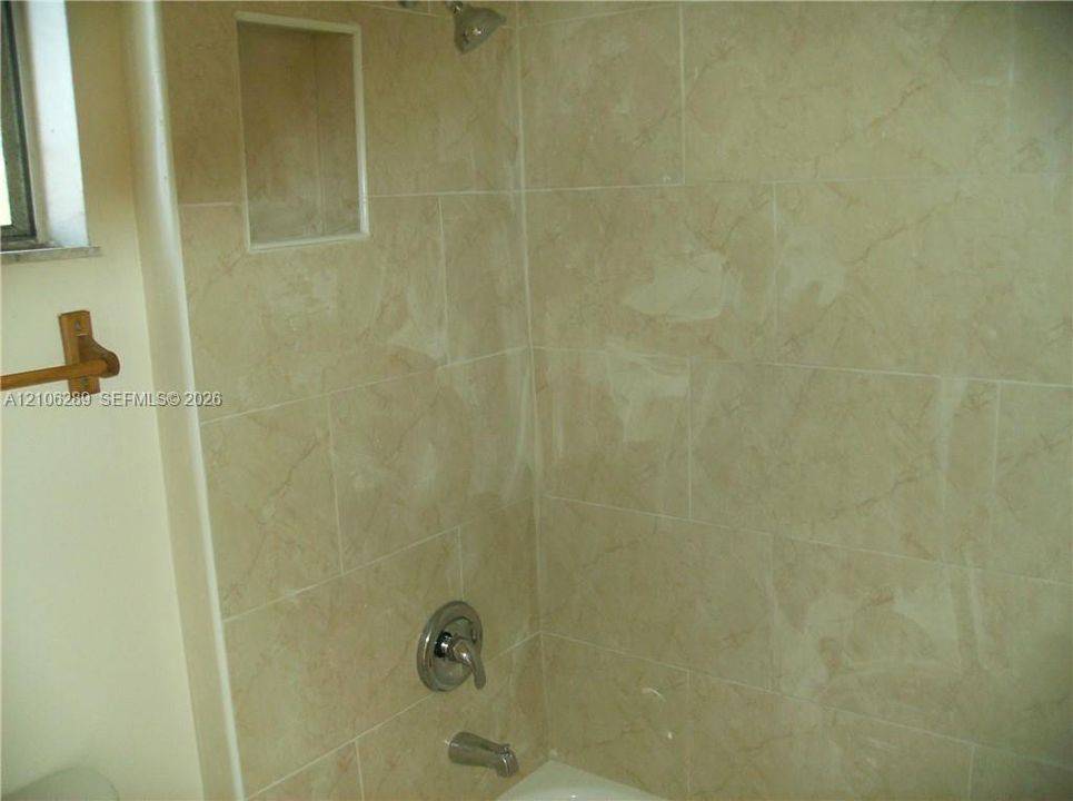 Full-height ceramic wall tiling featuring a neutral veined pattern, integrated recessed shelving, and a brushed metallic shower and tub faucet set